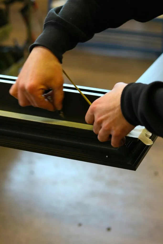 Hands measuring metal frame with precision in an industrial workspace.