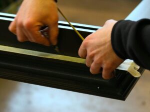 Hands measuring metal frame with precision in an industrial workspace.